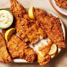 fried fish with lemon wedges and sour cream sauce on a plate next to another dish