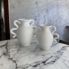 two white vases sitting on top of a marble table