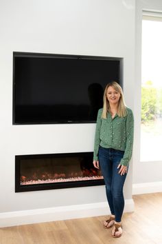 a woman standing in front of an electric fireplace