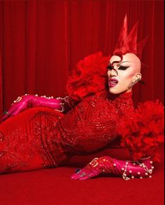 a woman with red hair and makeup laying on the ground in front of a red curtain