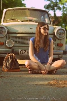 a woman sitting on the ground in front of a car