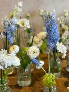 several glass vases filled with different types of flowers on a wooden table, one has white and blue flowers in it