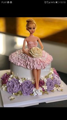 a barbie doll sitting on top of a cake with purple and white flowers around it