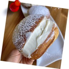 a person holding up a powdered donut with cream on it's side