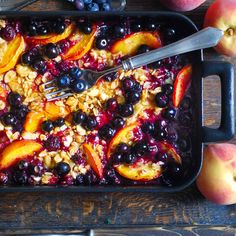 blueberries, peaches, and granola in a baking dish with a fork