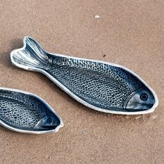 two metal fish shaped dishes sitting in the sand