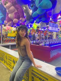 a woman sitting on top of a counter next to stuffed animals hanging from the ceiling