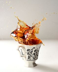 a cup filled with orange juice and splashing it into the air on a white surface