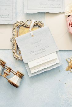 an assortment of wedding stationery items on a blue table with pink flowers and gold accents