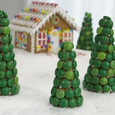 three small christmas trees made out of green candies and gingerbread house in the background