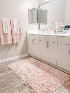 a bathroom with white cabinets and pink rug