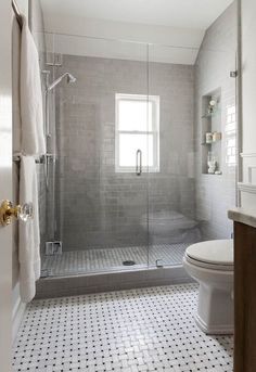 a white toilet sitting next to a shower in a bathroom under a window on top of a tiled floor