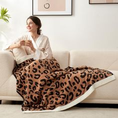 a woman sitting on a couch with a leopard print blanket over her lap and holding a cup