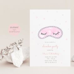 a pink sleeping mask on top of a white card next to some rocks and flowers