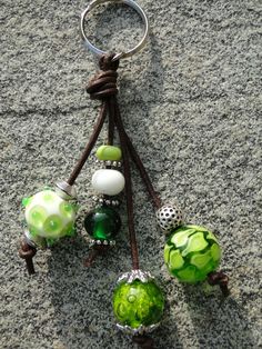 several green and white glass beads are hanging from a keychain on the ground