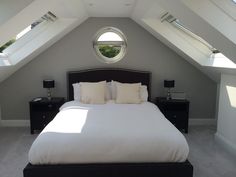 there is a large bed with white sheets and pillows in the room under the roof