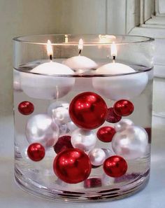 a glass candle holder filled with red and white christmas balls, floating candles and ornaments