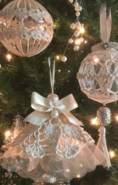 christmas ornaments are hanging from the tree with lights in the background and white bows on them