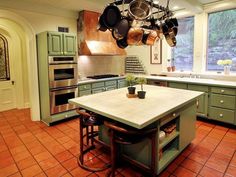 a large kitchen with green cabinets and pots hanging from the ceiling over an island counter