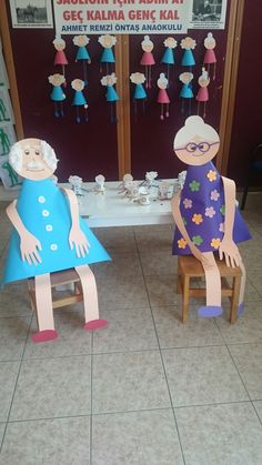 two paper dolls sitting on chairs in front of a table