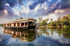 a house boat on the water with palm trees and clouds in the sky behind it