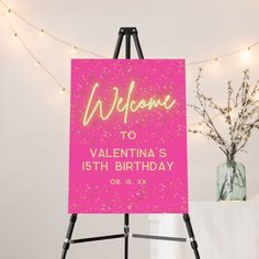 a pink welcome sign sitting on top of a easel next to a vase filled with flowers