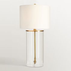 a glass lamp with a white shade on the top and gold trim around the base