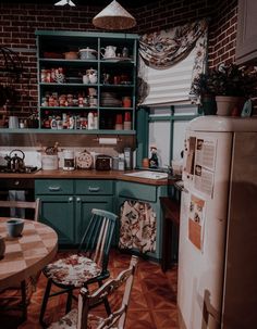 a kitchen filled with lots of green cabinets and wooden flooring next to a white refrigerator freezer