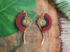 a pair of earrings sitting on top of a wooden table next to a green leaf