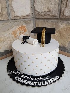 a white cake with black and gold decorations on it, decorated with a graduation cap and tassel