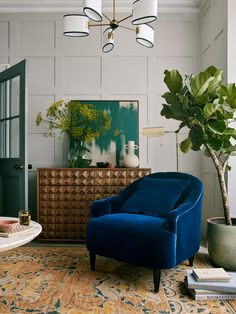 a living room with a blue chair and a potted plant on the sideboard