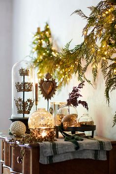 christmas decorations are displayed in glass domes on a table next to pine branches and garland