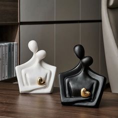 two black and white ceramic vases sitting on a wooden table in front of a bookshelf