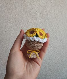 a crocheted cupcake with sunflowers is held in front of a white wall