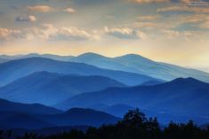 the mountains are covered in blue haze as the sun is setting over them and some clouds can be seen