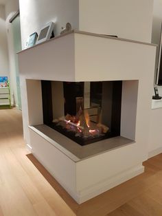 a modern fireplace in the middle of a living room with wood floors and white walls