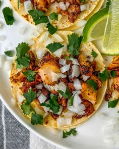 three chicken tacos with cilantro, onions and lime on a white plate