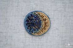 a blue and gold beaded brooch sitting on top of a white cloth covered surface