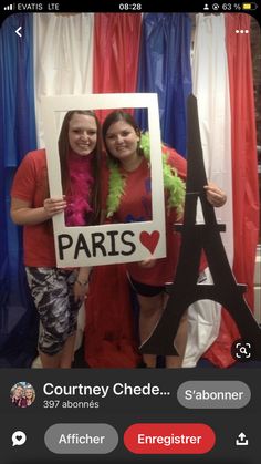 two women standing in front of the eiffel tower holding up a sign that says paris