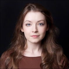 a woman with long brown hair is posing for a photo in front of a black background