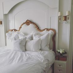 a bed with white linens and pillows in a small room next to two wall sconces