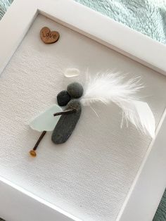 a white frame with some rocks and a feather on it, next to a heart