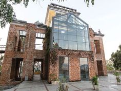 an old brick building with a glass roof and lots of windows on the outside, surrounded by greenery