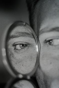 a man looking through a magnifying glass with his eye reflected in the lens