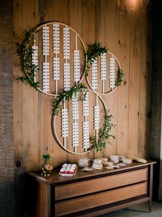 a wooden table topped with plates and cups next to a wall covered in greenery