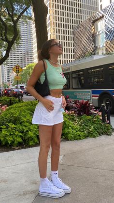 a woman standing on the sidewalk in front of a bus