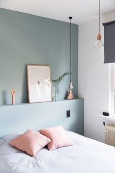 a bed with pink pillows on top of it next to a wall mounted light fixture