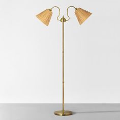 a brass floor lamp with two lamps on each side and a white wall in the background