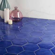 two vases sitting on a blue tiled countertop next to candles and a candle holder