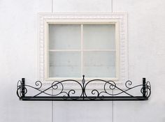 a window on the side of a white building with wrought iron bars and windowsill